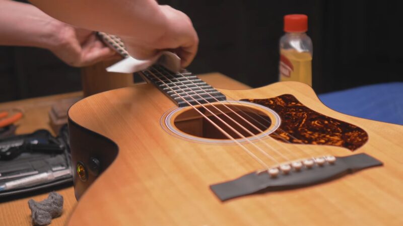 The man wipes each string individually on the guitar