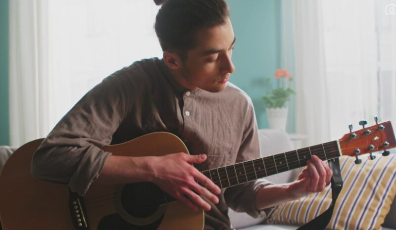 A young man plays an acoustic guitar