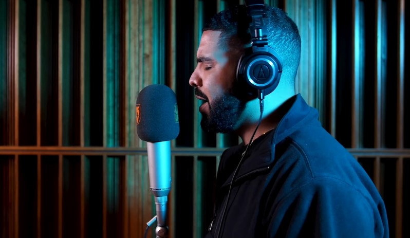 Drake wearing headphones in a studio and recording a track