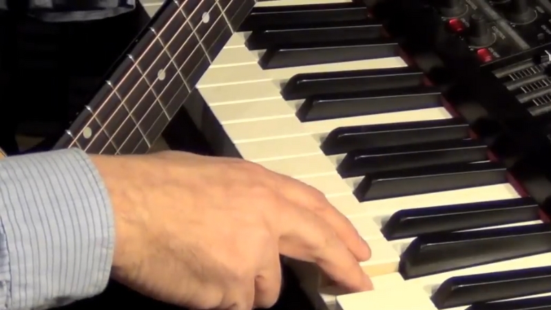 A Hand Pressing a Key on A Piano While Positioned Next to A Guitar's Fretboard