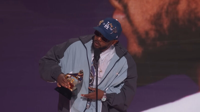 Kendrick Lamar holding a Grammy award while speaking at the microphone