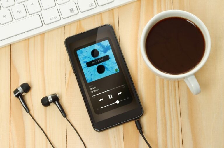 A smartphone displaying a music player app, with headphones and a cup of coffee nearby