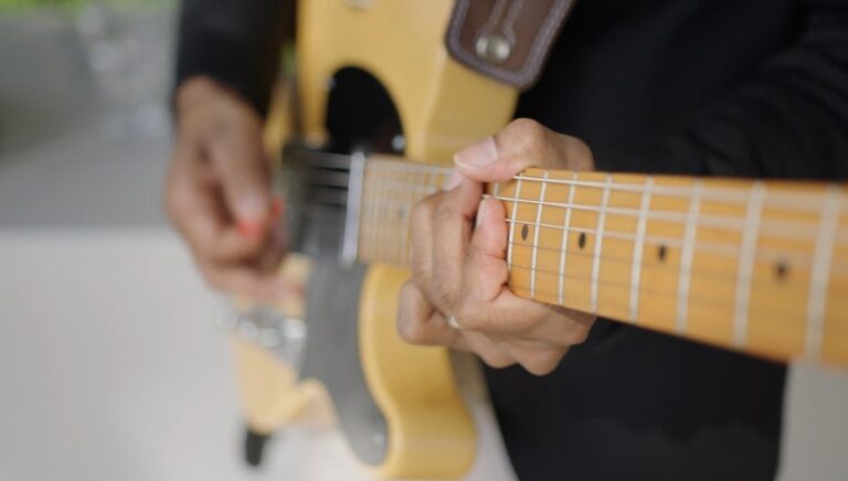 Close-up of a person's hands playing a light-yellow electric guitar