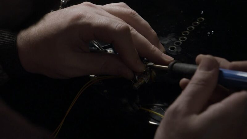 Close-up of a person soldering wires to a guitar component with a soldering iron