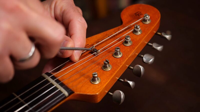 Close-up of a person using a small tool to adjust the string tree on a guitar headstock