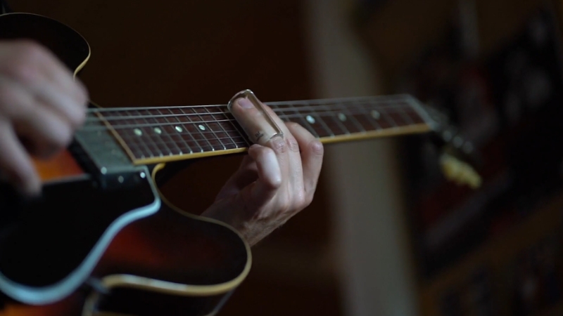 A close-up of a person playing guitar with a slide, showing focus and technique during practice