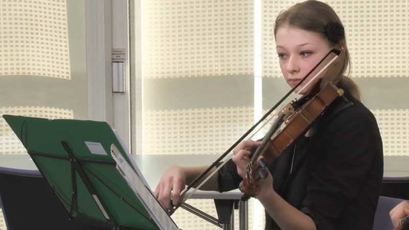 A young woman focuses intently as she plays the violin during a music practice session