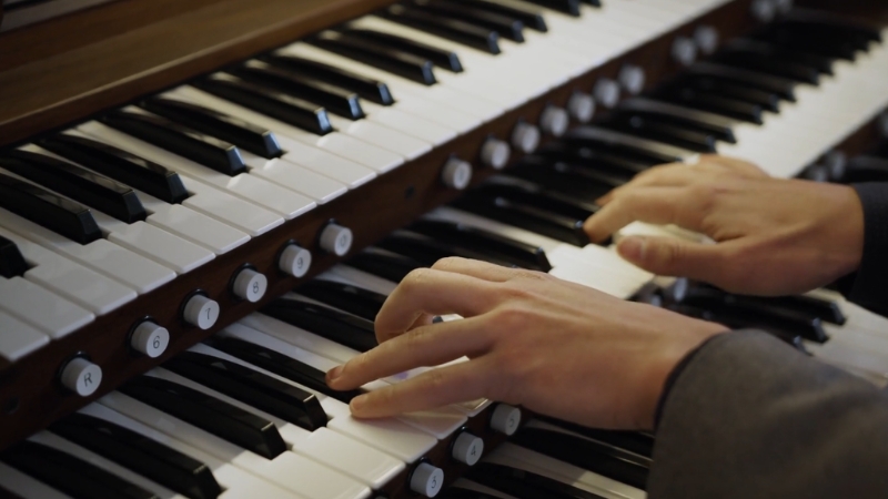 A person plays both manuals on a pipe organ, showing precise hand coordination