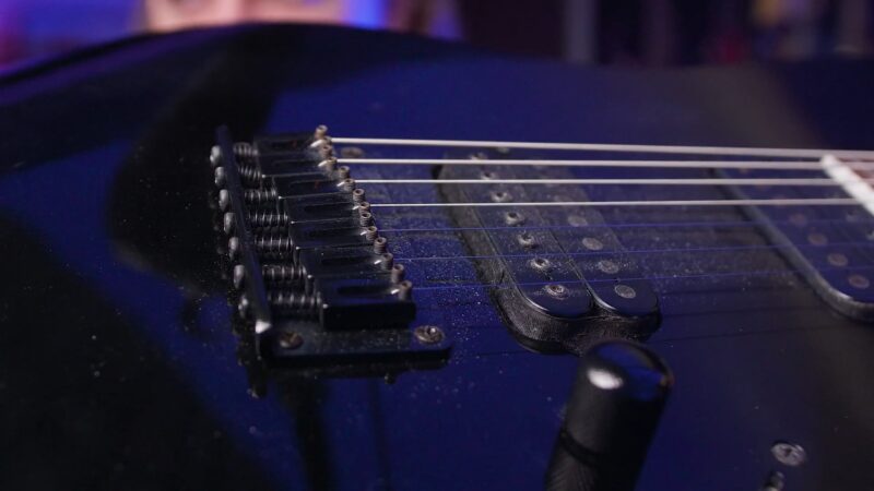 Macro shot of an electric guitar's pickups and bridge with visible strings and control knob