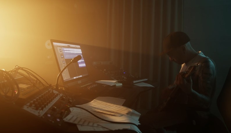 A musician engrossed in their craft, working on a musical composition in a dimly lit home studio