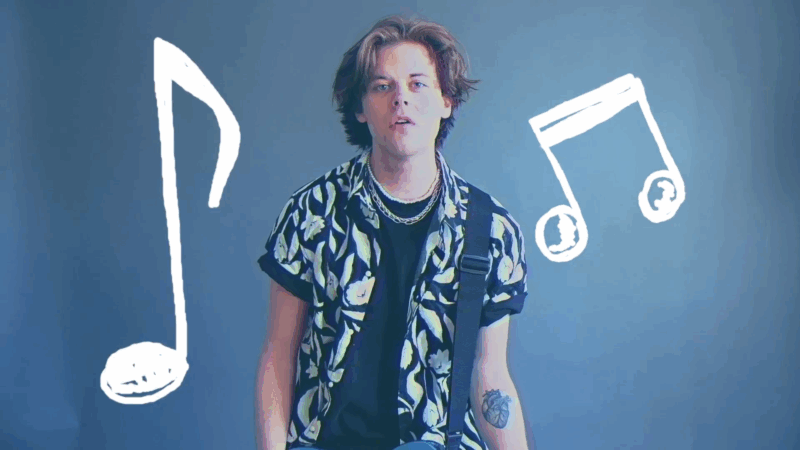 Alex Coles stands in front of a blue background with white music notes