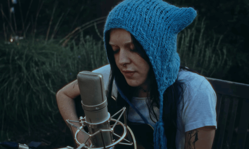 Ally Evenson plays guitar and sings into a microphone outdoors