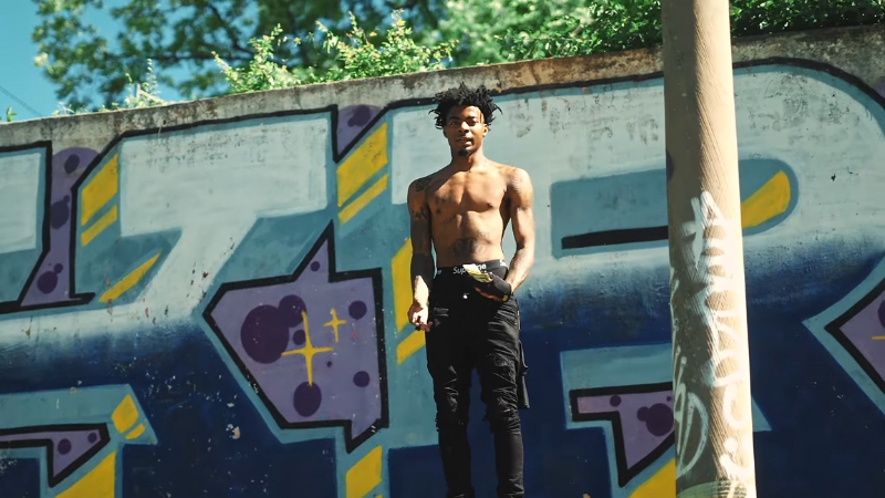 Lazer Dim 700 stands shirtless in front of a colorful graffiti wall during a street-style shoot
