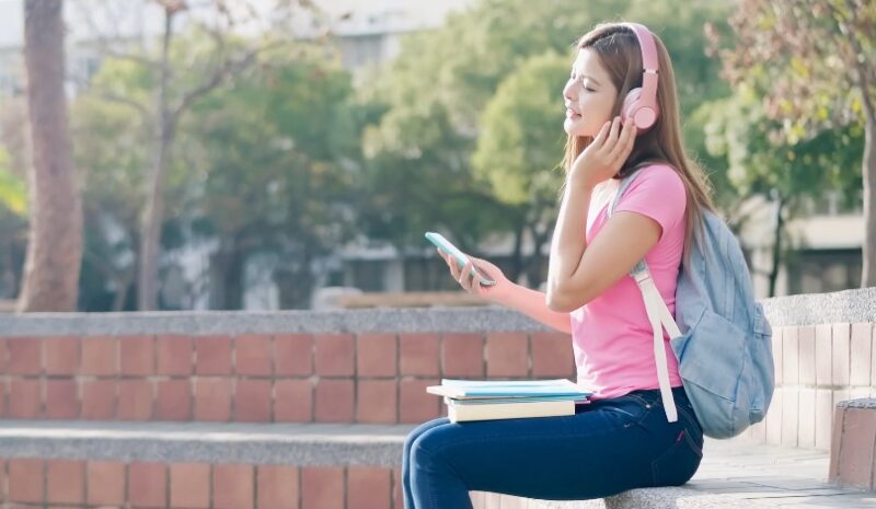 A young woman sits outdoors, listening to music on headphones