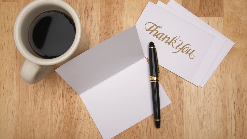 A cup of coffee sits next to blank thank you cards and a pen ready for writing messages of appreciation