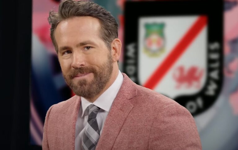 Ryan Reynolds, in a light pink blazer, displays a thoughtful expression