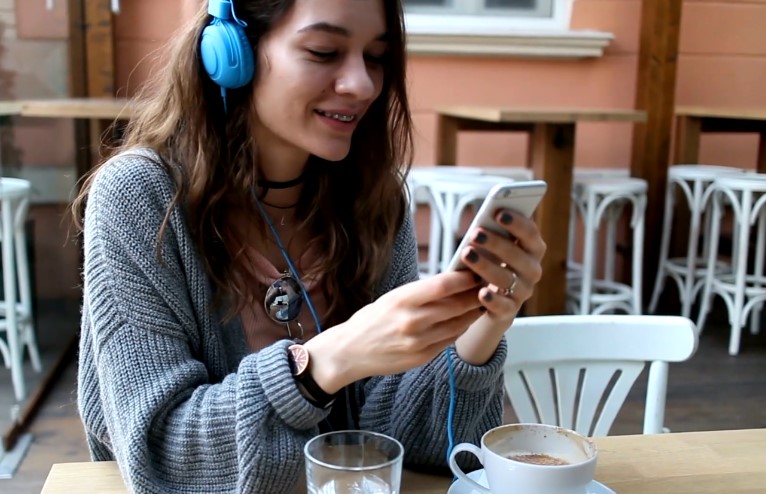 A young woman using a smartphone while listening to music in a cafe