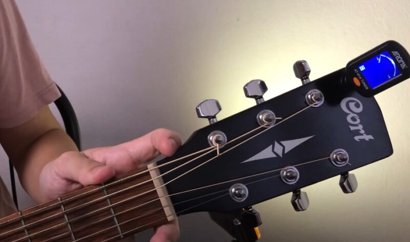 Close-up of a Cort acoustic guitar headstock with a digital tuner attached