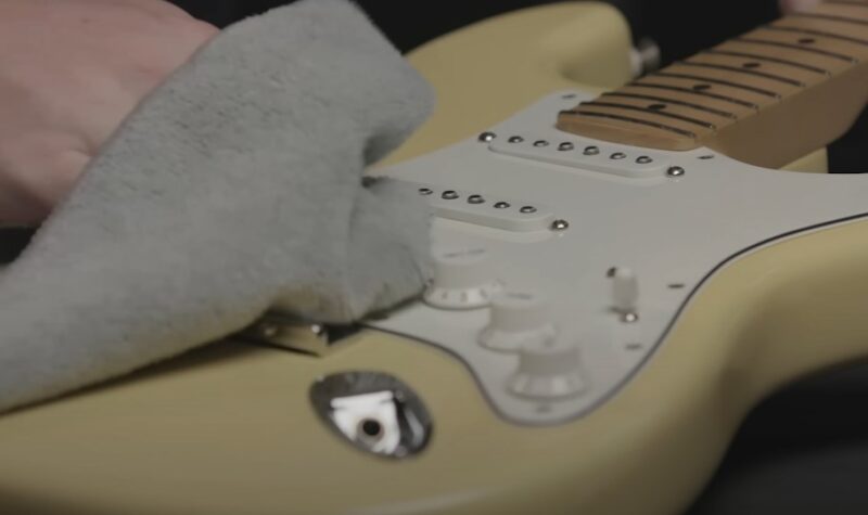 A soft cloth gently polishes the smooth surface of a cream-colored electric guitar