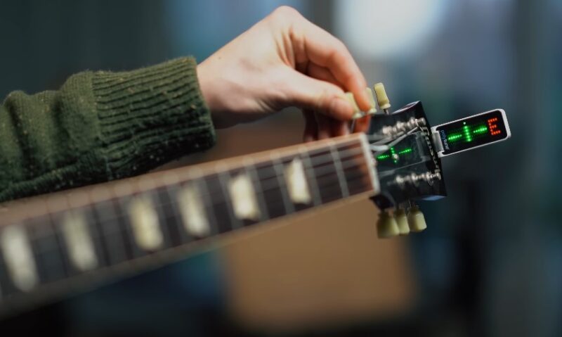 A person meticulously tunes a guitar, ensuring precise pitch with a digital tuner