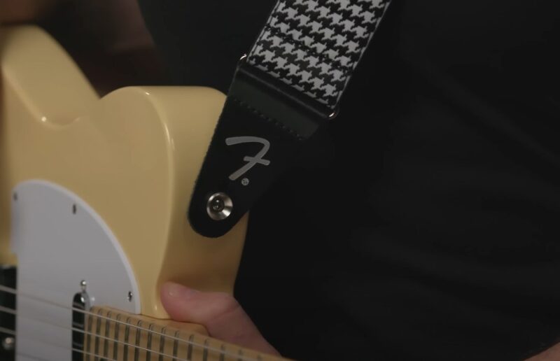 A cream-colored electric guitar, featuring a black and white houndstooth strap