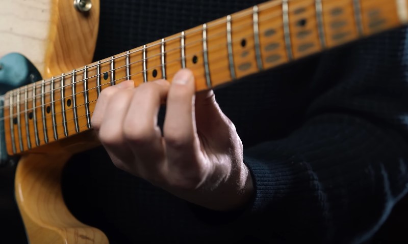 Musician's hand mastering a chord position on a guitar's rosewood fingerboard