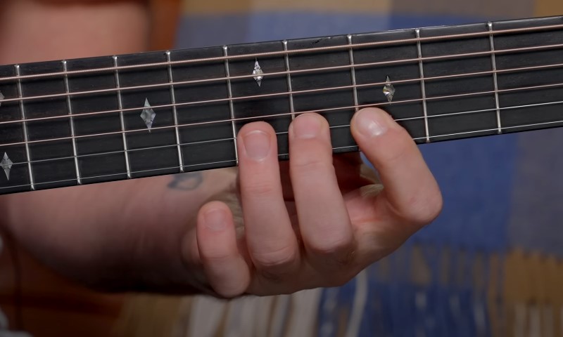 Fretting hand positioning on a guitar neck, showing precise finger placement on steel strings