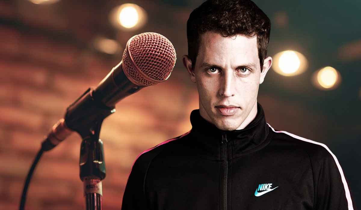 Man in a black Nike jacket standing in front of a microphone on stage with blurred lights in the background