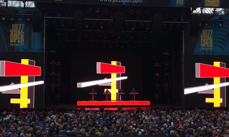 A large stage featuring a prominent screen displaying a red and yellow sign for Kraftwerk