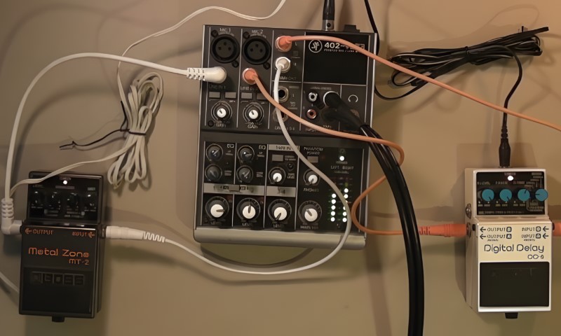 Interconnected music gear showcasing various white, orange, and black cables linking a mixer and two stompboxes